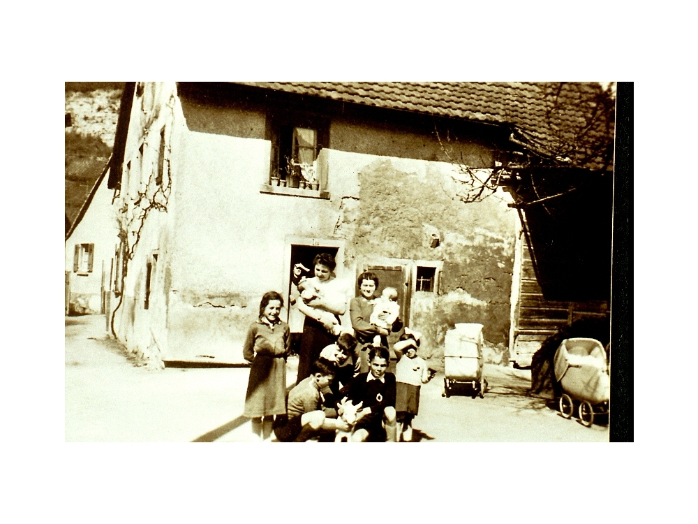 Haus Brucker in der Kirchstrasse. Hinten Reben und Steinbruch. Herrmann Brucker, Sattlermeisterca 1938, Schreinermeister Stöcklin vorne in schwarzem Pullover;in der Tür Rosine Brucker, mit Baby Frau Albiez  
Bild45